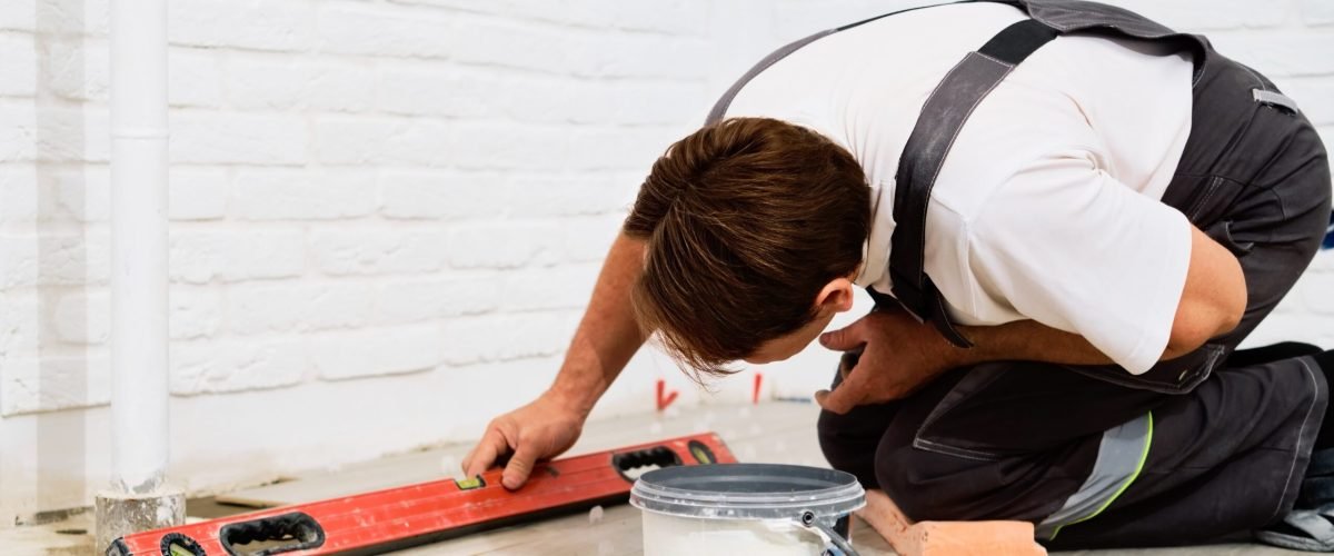 builder-checks-quality-laid-tiles-with-manual-bubble-level-construction-worker-installing-ceramic-floor-tiles-construction-sites-floor-repair-selective-focus-min